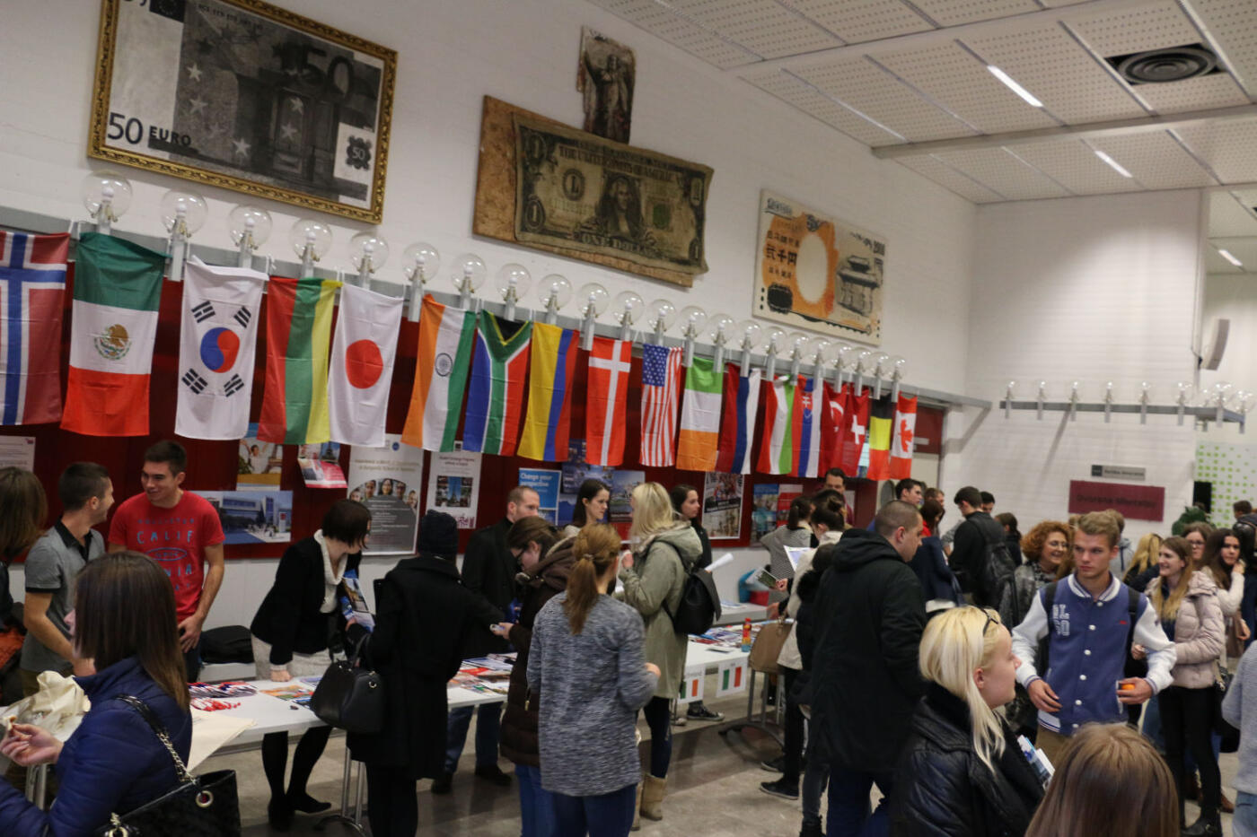 The auditorium is filled with students, with flags of different countries in the background.