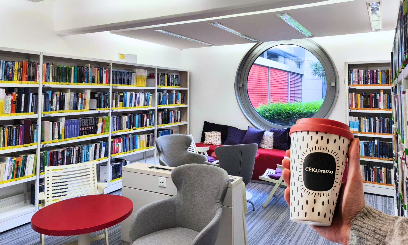 Roka drži kavni lonček z napisom »CEKspresso« v kotičku Knjižnice CEK, obkroženem s knjižnimi policami, naslanjači in okroglim oknom.
