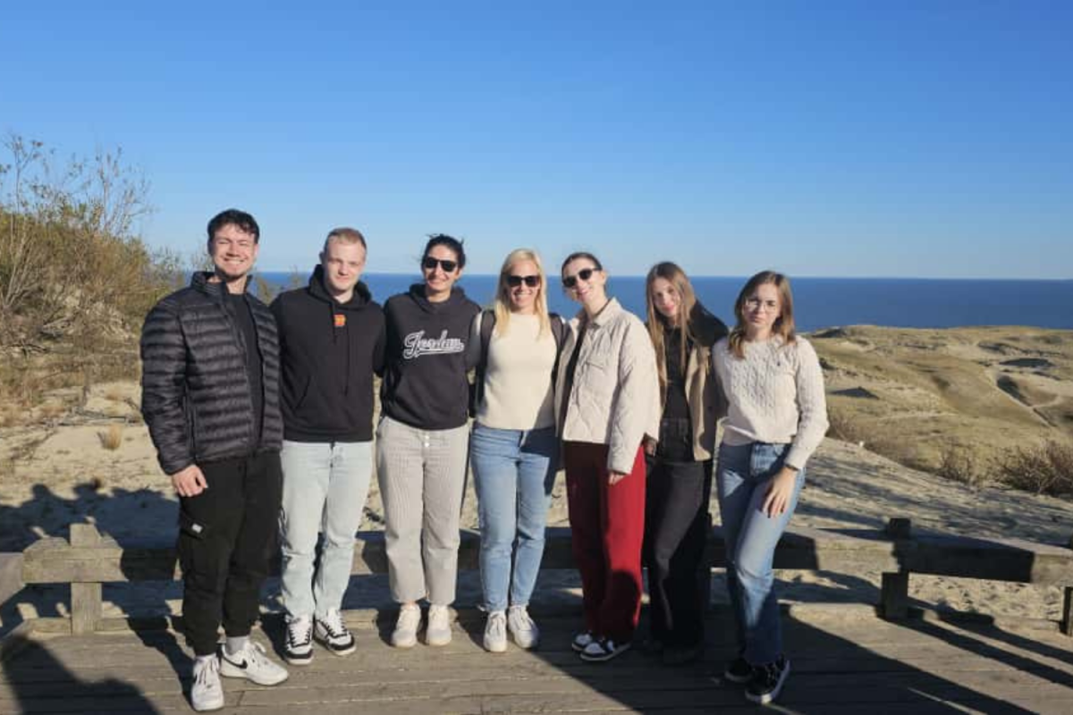 A group of people stands on a wooden boardwalk overlooking the ocean, enjoying the scenic view and each other's company.