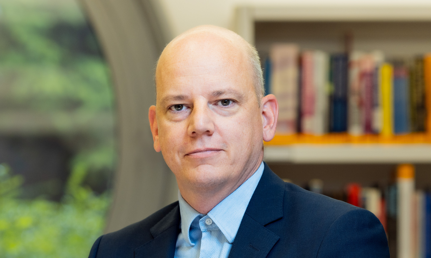 Poslovni portret Jake Cepca v prostorih knjižnice na Ekonomski fakulteti oktobra 2024, v ozadju okroglo okno in police s knjigami