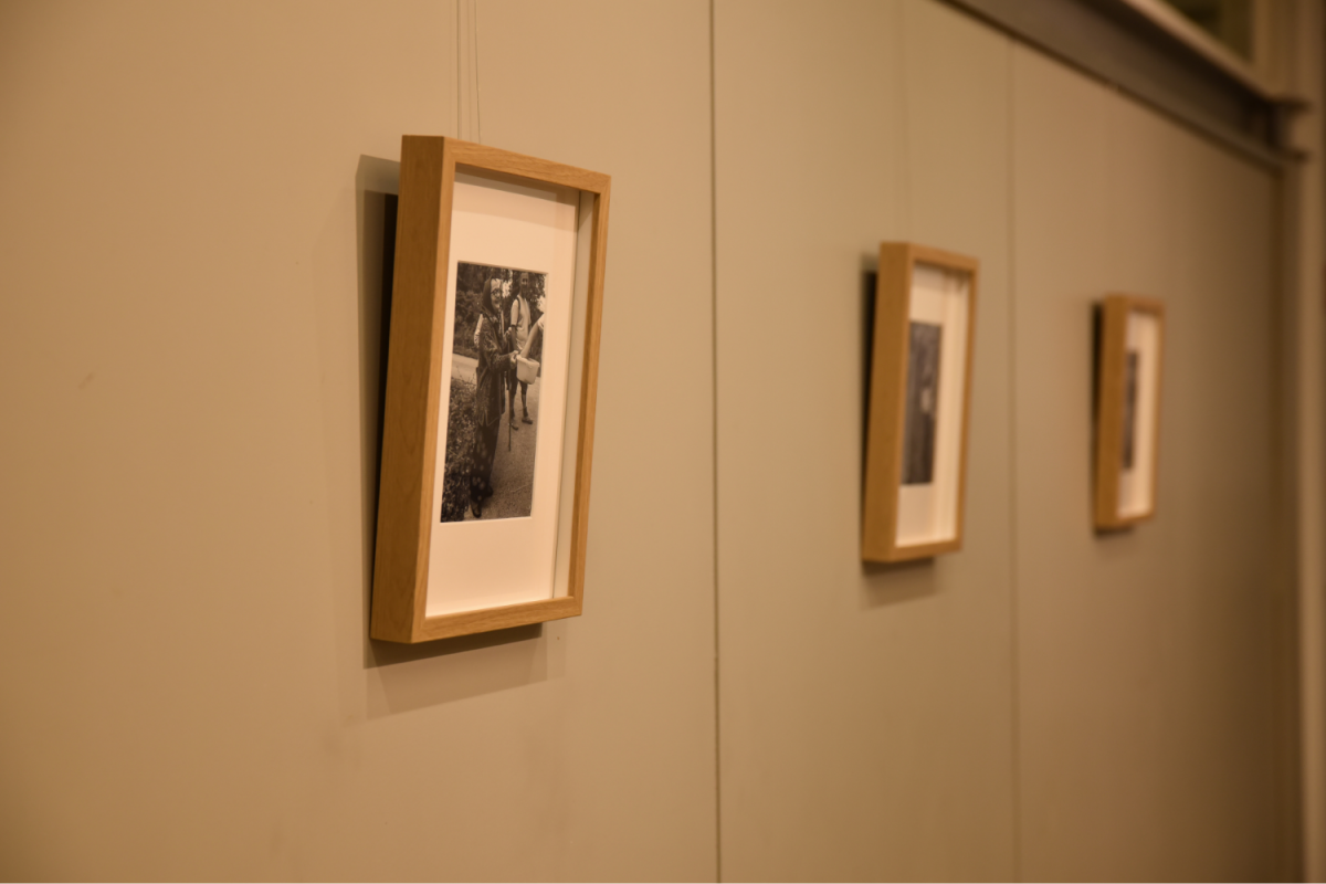 Na bež steni galerije visijo trije okvirjeni črno-beli fotografiji. Topla svetloba in leseni okvirji ustvarjajo prijetno, nostalgično vzdušje.