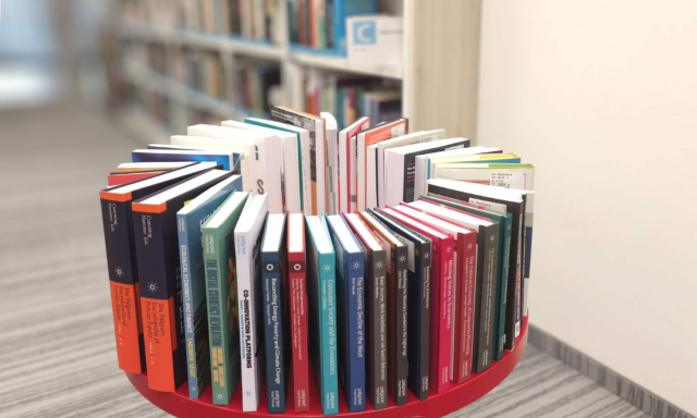 Photography of new books at the CEK Library displayed on a table in front of bookshelves; titles from Palgrave Macmillan on money and finance and labour economics predominate.