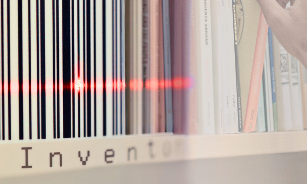 Photo showing a barcode and a red laser beam on the left side, blending into a bookshelf with books and a hand reaching for one of them on the right. The shelf displays the word "Inventory".