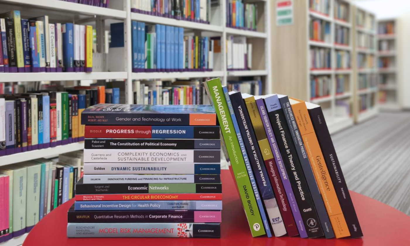 A selection of new academic books at the CEK Library displayed on a table in front of bookshelves, predominantly titles published by Cambridge University Press in the fields of economics, finance and management.