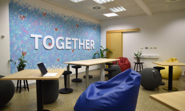 Udobna soba s pisanimi sedežnimi vrečami, majhnimi mizami in modro stensko poslikavo z napisom »TOGETHER« v krepkih črkah. Svetla, prijetna in sodelovalna atmosfera.