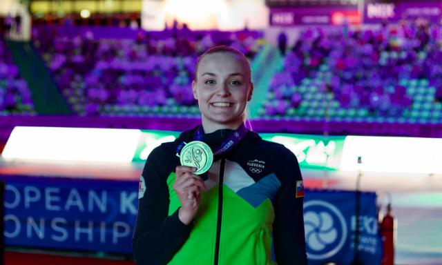 Ženska ponosno drži medaljo pred navdušeno množico, ki proslavlja njen dosežek.