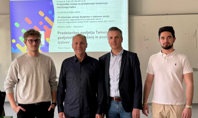 Four men stand side by side in front of a screen displaying text. They appear confident and casual, suggesting a presentation or meeting setting.