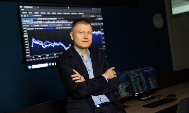 Moški v obleki sedi za mizo in se v profesionalnem okolju osredotoča na zaslon računalnika.