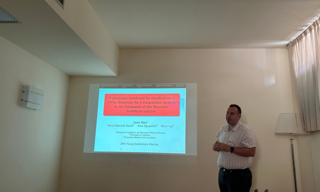 Moški stoji ob projekcijski sliki z naslovom »Prototip nadzorne plošče za vizualizacijo KPI-jev«. Prostor je nežno osvetljen in izžareva profesionalnost.