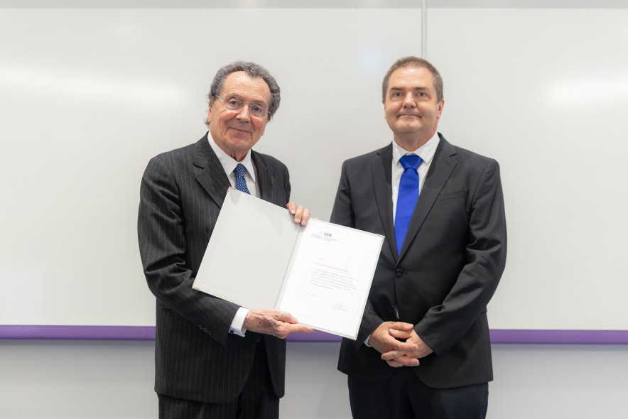  Prof. Gian Maria Gros-Pietro with a plaque in his hands, next to him Prof. Tomaž Turk, Dean of UL SEB, a white school board in the background.