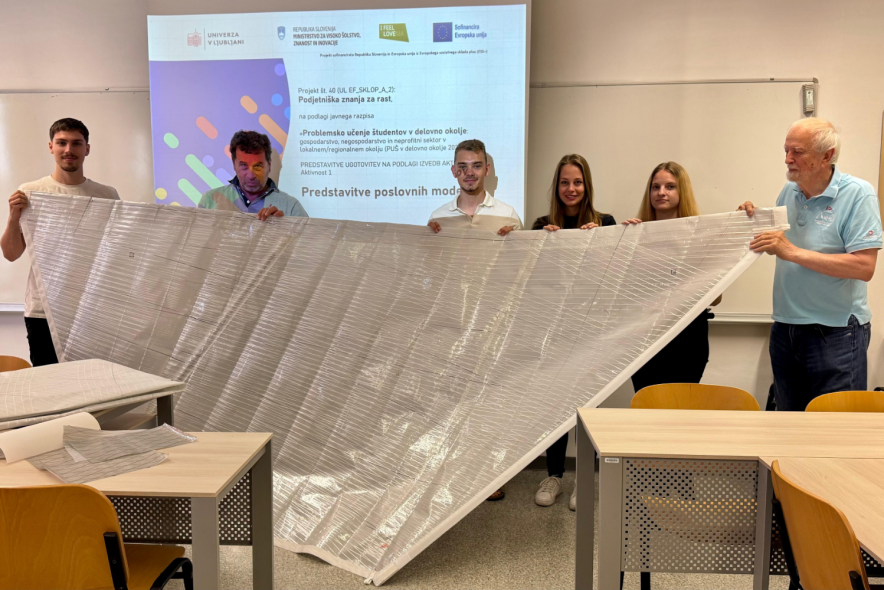 Skupina ljudi stoji skupaj pred projektorjem in predstavlja svoj produkt. 