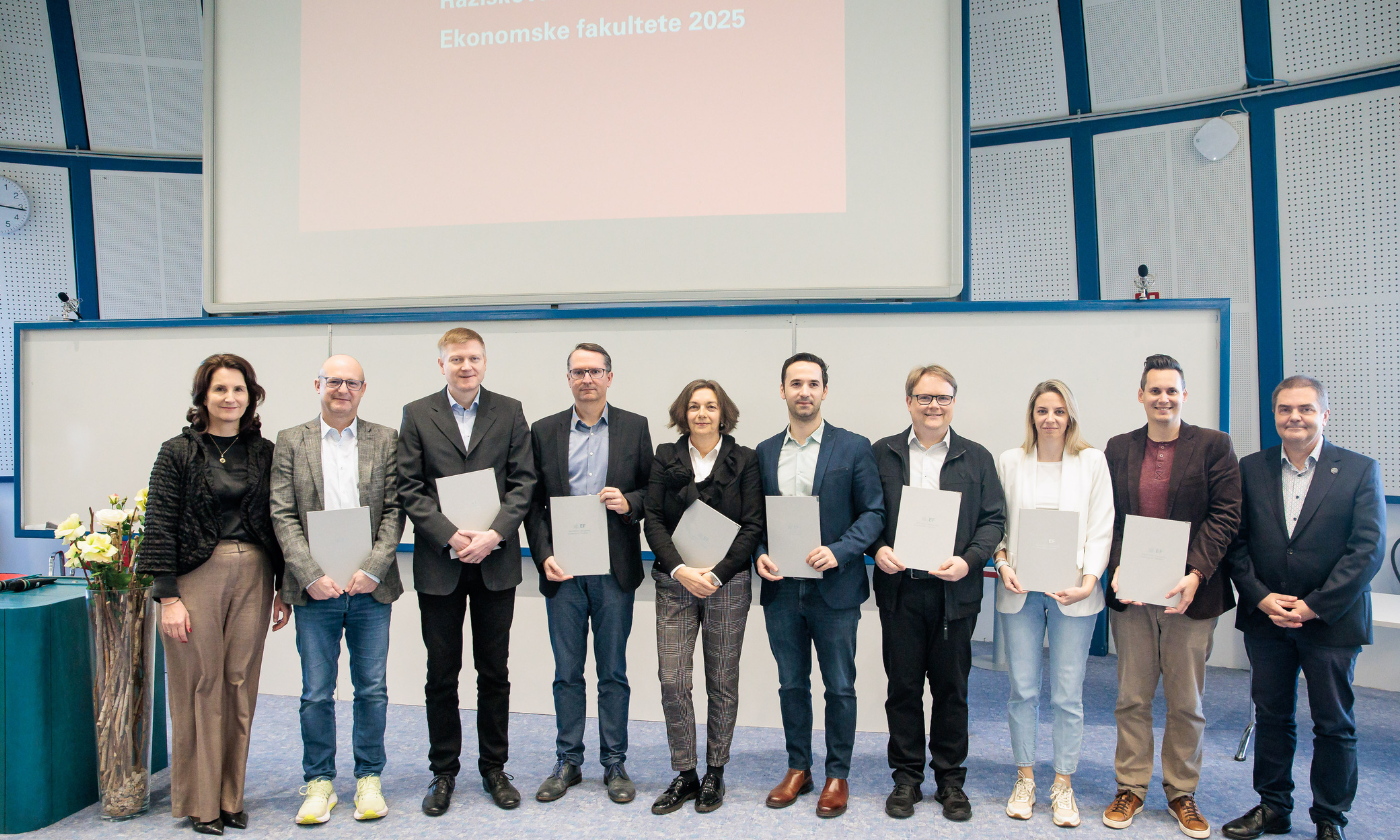 Skupina raziskovalk in raziskovalcev z nagradami pred belo tablo na katedru Plave dvorane Ekonomske fakultete. 