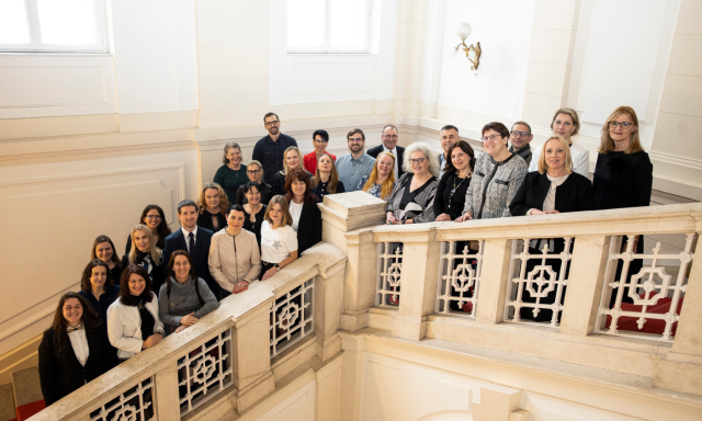 Skupina ljudi stoji na stopnicah stavbe, se smeji in pozira za fotografijo.