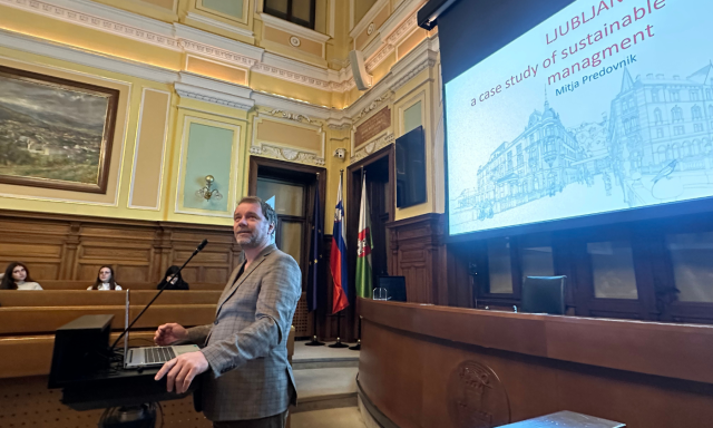 A man stands in front of a large screen in a courtroom, engaged in a presentation.