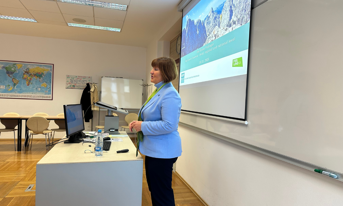 A woman stands in front of a classroom screen, engaging with students during a lesson.