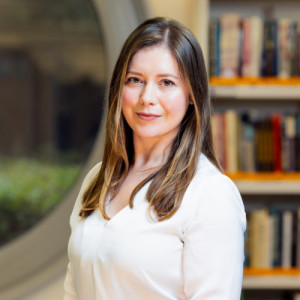 Poslovni portret Mojce Svetek v prostorih knjižnice na Ekonomski fakulteti oktobra 2024, v ozadju okroglo okno in police s knjigami