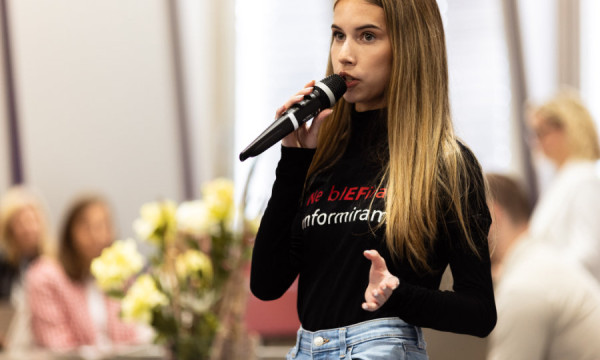 A female student speaks into a microphone and addresses students at an information day.