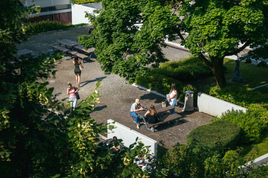 Ptičja perspektiva študentov, eni sedijo za mizo v atriju, drugi pa se sprehajajo.
